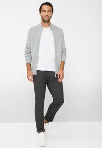 Grå strikket cardigan med ribbede manchetter og krave, parret med hvid t-shirt og mørkegrå bukser, afsluttet med hvide sneakers.