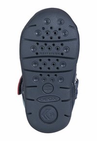 Suela de goma negra con múltiples orificios de drenaje, que presenta el texto "Flexy System". El lateral tiene un patrón texturizado con el logo "GEOX" y el sello de patente italiana.