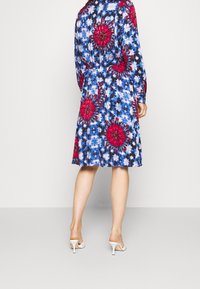 Robe à motifs floraux en bleu, rose et blanc ; à manches longues, taille cintrée, longueur genou, en tissu léger, avec une coupe décontractée.
