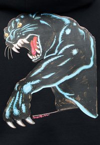 Pantera negra con manchas azules brillantes, ojos amarillos, boca abierta mostrando dientes afilados y lengua rosa, rugiendo con una pata extendida y con garras.