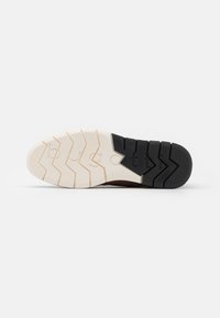 Shoe sole with a segmented design featuring a beige surface and black accents, textured for grip with a zigzag pattern.