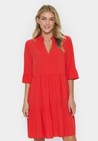 Robe rouge patin longueur genoux avec un décolleté en V et des manches à volants. Fabriquée en tissu léger, elle présente un design à plusieurs niveaux et une texture lisse.