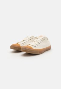 Canvas sneakers in off-white with rubber soles. Rounded toe with a tan cap, featuring white laces and subtle branding on the tongue.