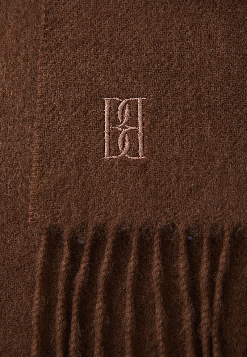 Brun ullscarf med fransade kanter och rosa broderade sammanflätade bokstäver "D" och "H" i mitten.