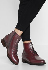 Bordowe skórzane botki na kostkę z okrągłym noskiem, sznurowadłem i zapięciem na zamek, oraz teksturowaną podeszwą. Posiadają akcenty w postaci przeszyć dla większego detalu.