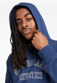 Felpa blu navy in misto cotone, con logo frontale "New Balance Athletics", cappuccio con cordino e polsini a costine.