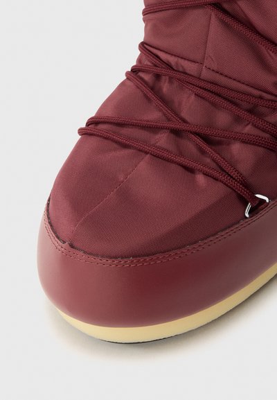 Zapato burdeos hecho de un textil resistente con suela de goma suave. Presenta puntera redondeada, superficie texturizada y un intrincado diseño de cordones.