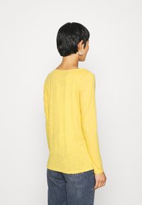 Langärmliges gelbes Shirt aus leichtem, strukturiertem Stoff mit lockerer Passform und Rundhalsausschnitt, von hinten gezeigt.