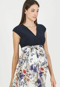 Haut navy avec un col en V et des manches courtes, se terminant par une jupe à motifs floraux blancs, avec des bleus et des roses éclatants, nouée à la taille.
