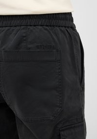 Black cargo pants featuring an elastic waistband, side pockets, and textured fabric with a visible brand logo on the back pocket.