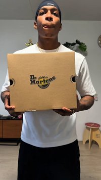 Cutie maro de carton cu logo-ul "Dr. Martens" imprimat negru, conținând decupaje în formă de mâini, cu un luciu ușor, de formă dreptunghiulară.