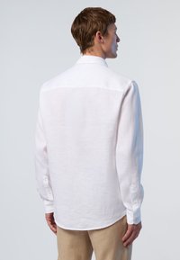Camicia bianca di lino con yoke posteriore, maniche lunghe, polsini con bottone e orlo curvo, che mette in mostra un tessuto leggero e strutturato.