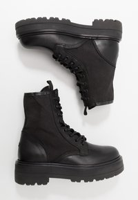 Schwarze Knöchelstiefel aus Leder und Stoff, mit Schnürdesign, klobiger Sohle und strukturierten Akzenten im Obermaterial.