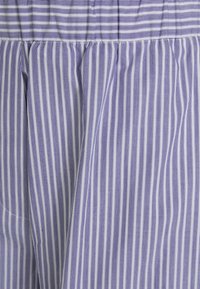 Pruhovaná látka v světle modré a bílé, s úzkými svislými pruhy. Materiál vypadá hladce s mírným leskem a detaily na staženém pase.