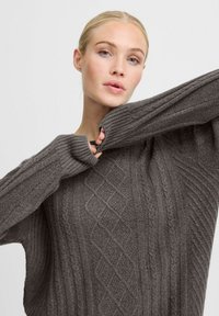 Grauer Strickpullover mit strukturiertem Design, ausgestattet mit gerippten Ärmeln und einem Rautenmuster am Körper. Weicher Stoff und lockere Passform.