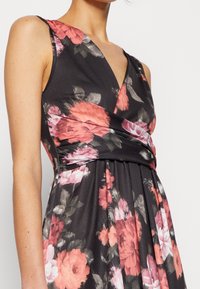 Blommig klänning med svart bakgrund, med djup V-ringning, utan ärmar och plisserad kjol med rosa och röda blommönster.
