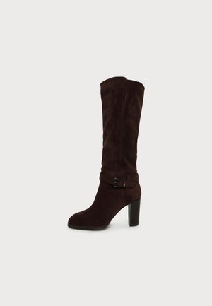 Botte haute en daim marron foncé avec talon bloc et bride décorative à boucle sur fond clair uni.