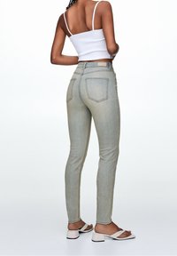 Jeans de mezclilla azul claro con un ajuste skinny, que presentan bolsillos traseros y una cintura de altura media. Combinados con un top corto blanco y sandalias.