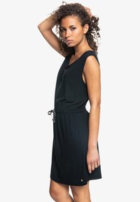 Vestido negro sin mangas con cintura ajustable, tejido suave y corte holgado, con un pequeño logo cerca del dobladillo.