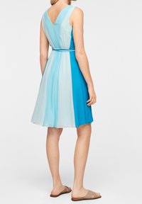 Une robe sans manches présentant un décolleté en V, dans un dégradé de bleu clair et de turquoise, avec une taille cintrée et un tissu doux et fluide.
