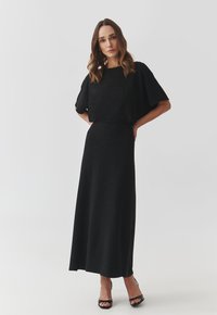 Schwarzes, gestricktes Zweiteiler-Kleid mit einem kastigen Oberteil und weiten Ärmeln sowie einem langen, schlichten Rock. Glatte Textur mit fließender Silhouette.