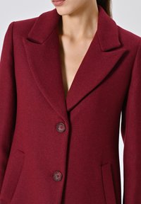 Bordeaux wollen blazer met een pieklapels, twee knopen en zijzakken. De gestructureerde stof verleent het een rijke, warme uitstraling.