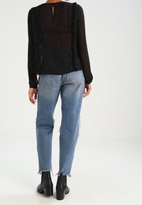 Sort bluse med polka dot mønster og flæser i siderne, parret med lyseblå slidte jeans og sorte ankelstøvler.