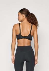 Sutien sport negru cu bretele reglabile, material neted și închidere cu cârlig la spate, asociat cu colanți negri cu talie înaltă.