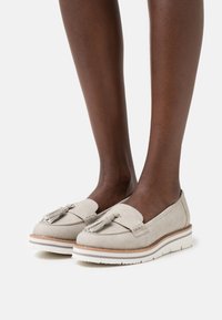 Beige textured loafers with tassels, a rubber sole, and white accent stitching. Designed for comfort with a sleek silhouette.