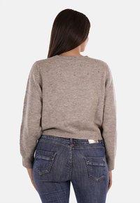 Maglione lavorato a maglia di un beige chiaro con scollo rotondo, tessuto testurizzato e sottili dettagli di perle sulla schiena, abbinato a jeans blu scuro.