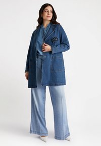 Palton din denim cu un design clasic, având două buzunare frontale, un accent floral și o croială lejeră, asortat cu blugi largi de culoare albastru deschis.