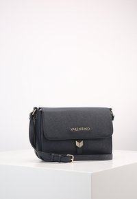 Black leather crossbody bag with a textured finish, gold hardware, flap closure, and adjustable strap. Features logo prominently displayed.