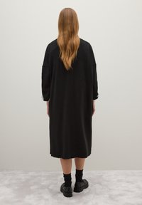 Abito in maglia oversize nero con maniche lunghe, taglio al ginocchio e spacchi laterali. Abbinato a scarpe con piattaforma nere e calzini alla caviglia.