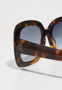 Gafas de sol de gran tamaño de carey con lentes gris degradado, que presentan un acento de logo dorado en el brazo lateral. Acabado suave y brillante.
