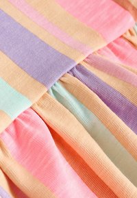 Gros plan d'un tissu doux avec de larges rayures pastel en rose, violet, pêche et bleu clair, montrant la texture et les détails des coutures froncées.