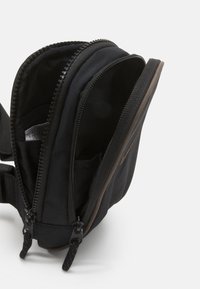 Černá textilní crossbody taška s dvojitými zipy, texturovanými popruhy a vnitřními kapsami. Kompaktní design vhodný pro různé malé předměty.