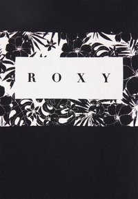Tela negra con una etiqueta rectangular blanca que dice "ROXY", rodeada de patrones florales tropicales en blanco y negro.