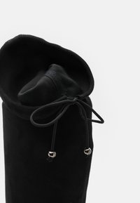 Botas de ante negras con una parte superior suave y enrollada y un cierre de cordón, que presentan detalles en plata para ajustabilidad.