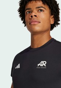 Svart atletisk t-shirt med korta ärmar, med en vit logotyp "AR" och tre ränder design på vänster sida, tillverkad av ett mjukt material.
