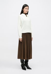 Κρέμα πλεκτό πουλόβερ με γιακά συνδυασμένο με καφέ πλισέ φούστα και μαύρες κλειστές μπότες μέχρι το γόνατο. Λείες υφές και στρωματοποιημ�ένο σχέδιο.