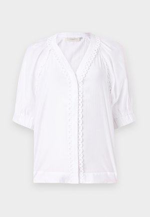 Blouse blanche avec des manches courtes bouffantes, décolleté en V, bordure festonnée le long de la patte de boutonnage et texture de tissu lisse. Aucune fermeture visible.