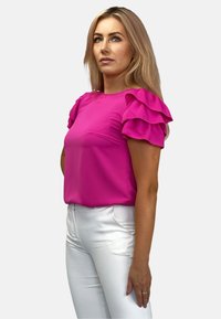 Fuksjowa bluzka z krótkim rękawem z warstwowym krojem falbany; gładka tekstura. Połączona z białymi dopasowanymi spodniami z delikatnym połyskiem.