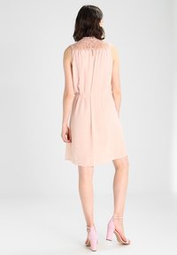 Robe rose blush avec un col crocheté, sans manches, taille cintrée et jupe fluide. Accompagnée de sandales à talons roses assorties.