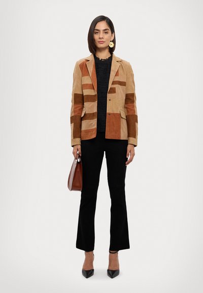 Blazer in suede marrone e beige con blocchi di colori geometrici, rever, due tasche anteriori, abbinato a un top nero testurizzato e pantaloni neri a campana.