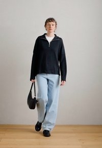 Sweater preto com fecho, branco por baixo, jeans azul claro, mala de ombro preta e sapatos pretos. Textura suave, corte descontraído, design minimalista.