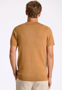 Lyhythihainen, pyöreäkauluksinen neulepaita sinapinkeltaisena, valmistettu pehmeästä, teksturoidusta kankaasta. Varustettu ribbikuvioiduilla hihoilla ja helmalla, rento mitoitus.