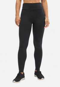 Leggings negros de cintura alta con una textura suave y un diseño ajustado, combinados con zapatillas deportivas negras. Detalles de costura a lo largo de las piernas.