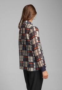 Sheer checkered jacket in shades of navy, cream, and red, featuring a collar and ribbed cuffs. Loose fit with a lightweight texture.