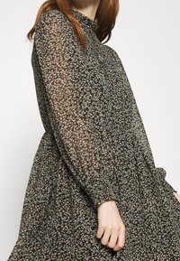 Robe florale en tissu transparent noir, avec des manches longues et une taille froncée. De petites fleurs bleues et roses forment un motif en tout point.