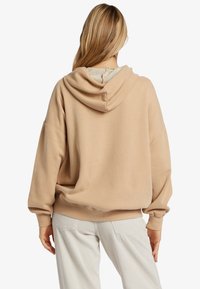 Sudadera oversize beige con capucha ajustable y puños acanalados. Forro interior suave, combinada con pantalones de pana clara.